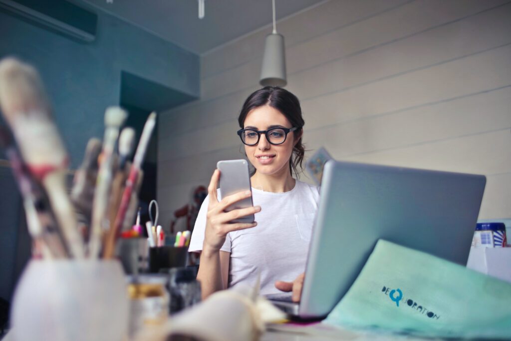 woman behind a laptop, using a mobile phone