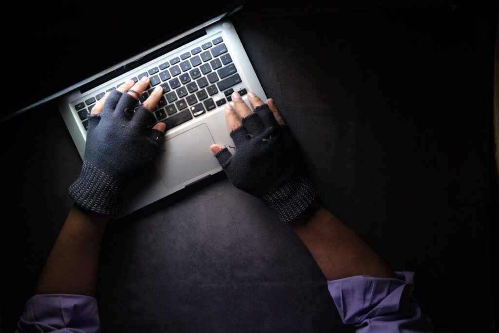a man wearing fingerless gloves and rolled up sleeves types on a laptop keyboard