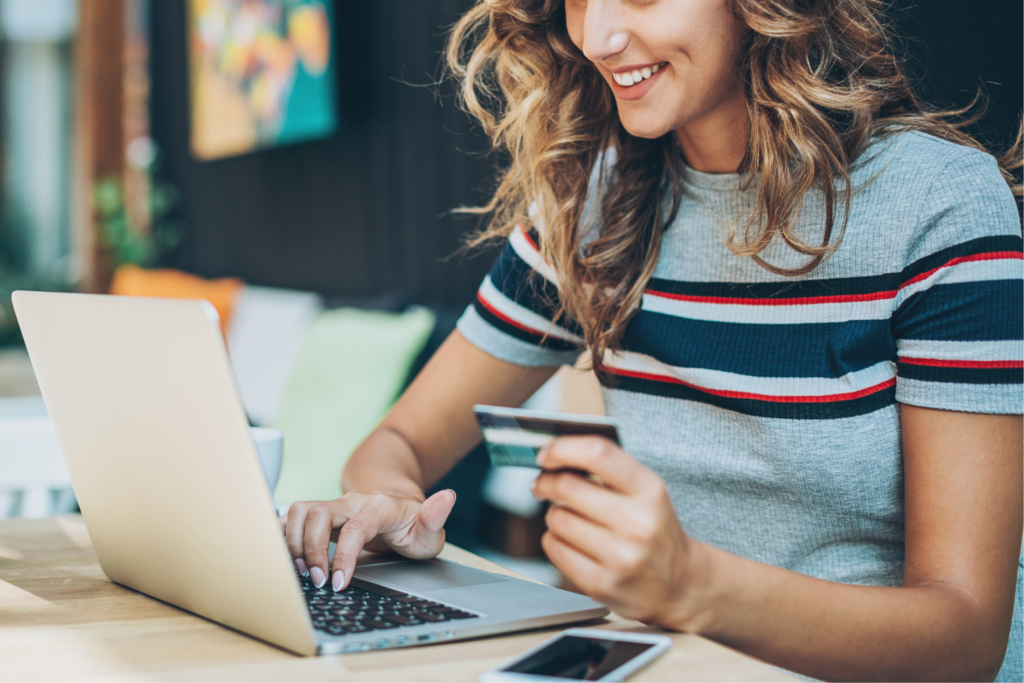 a woman happily prepares a bank card beside a computer, to make an online purchase