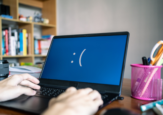a blue laptop screen showing a sad face emoji