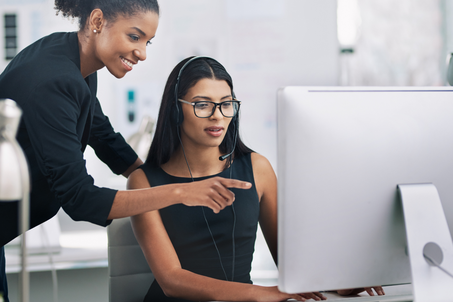 a woman professional shows a colleague something on their screen.