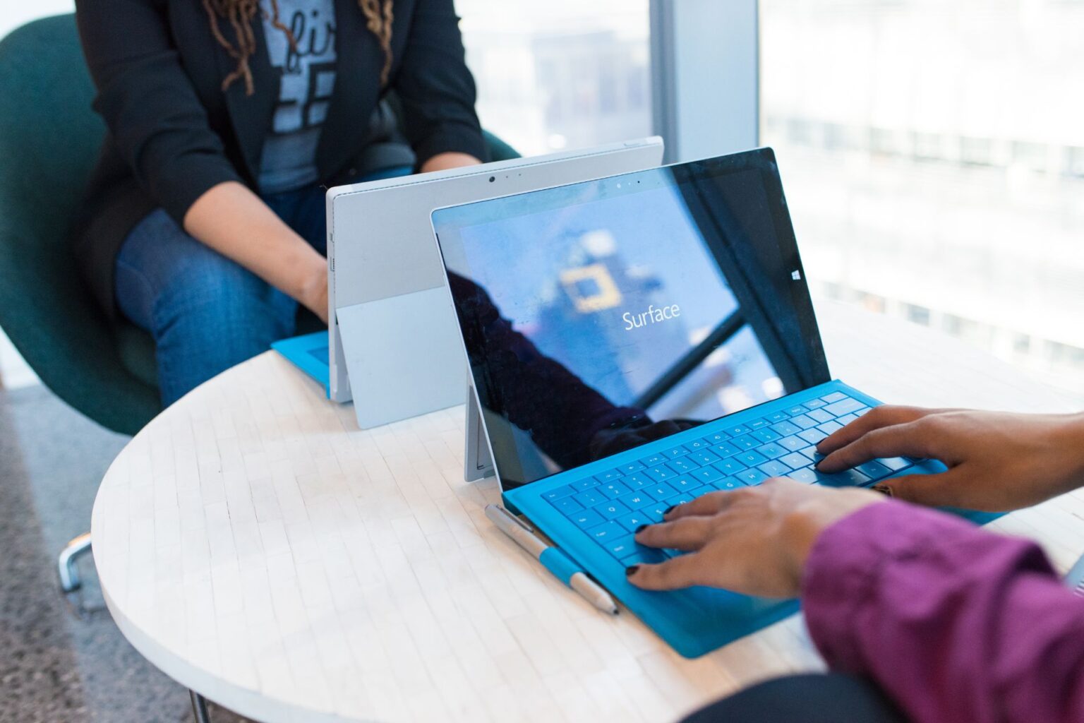 two professional women working on a small desk, using Microsoft Surface tablets
